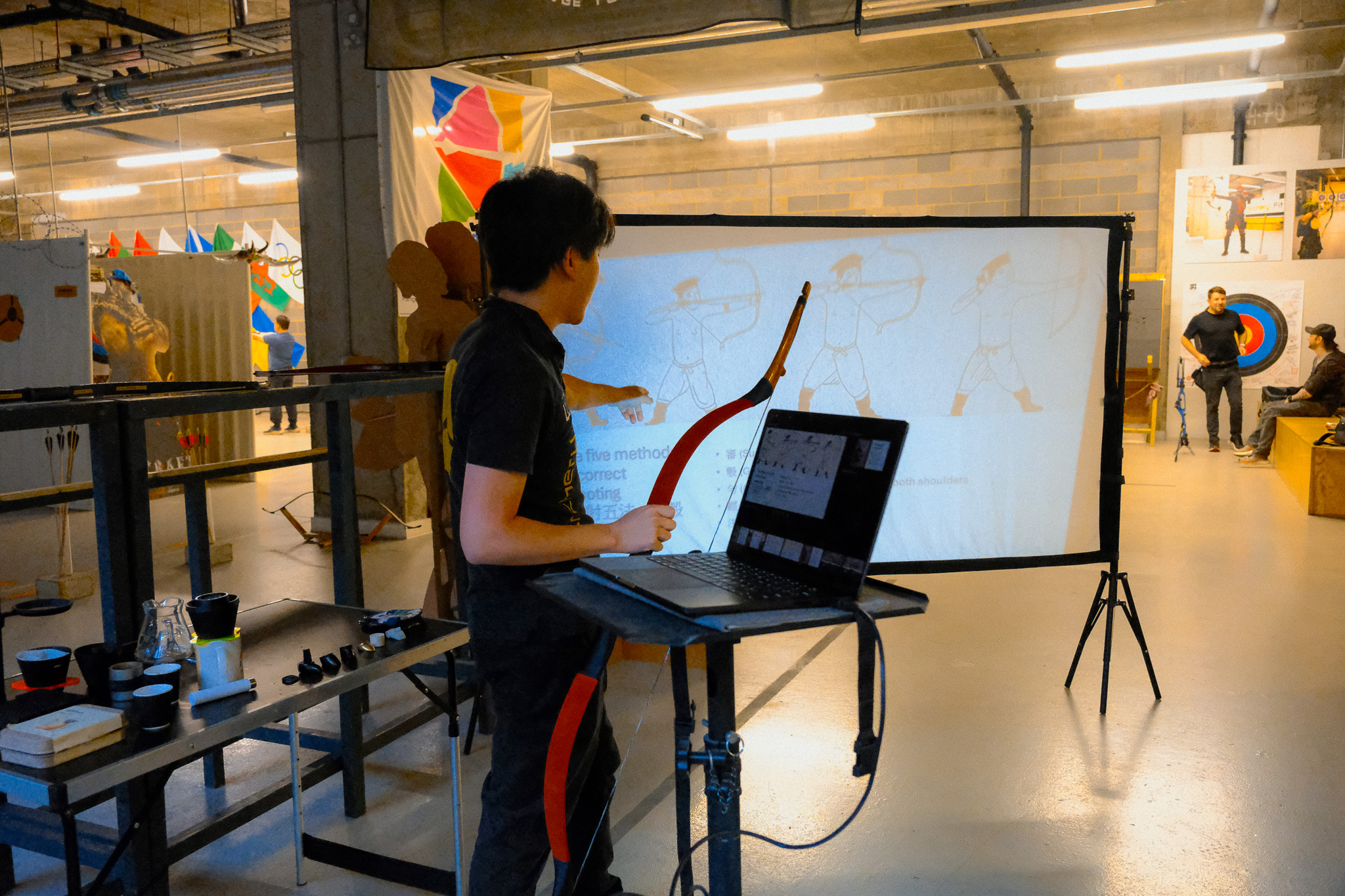 A coach reviewing archery technique slides on a projection screen during a form-check session