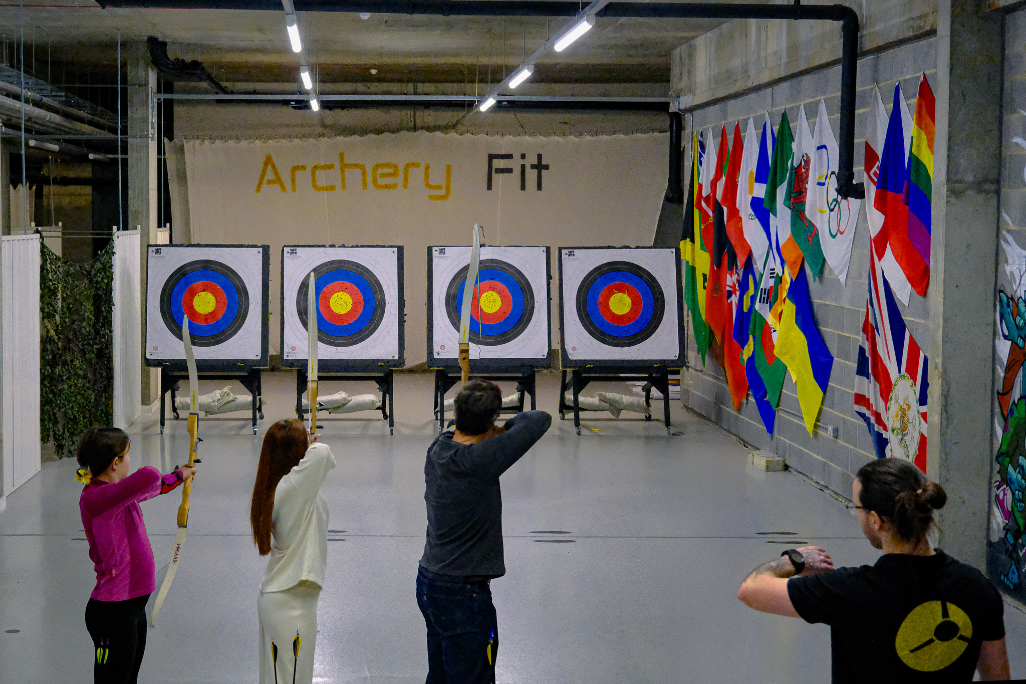 Archers at full draw on Archery Fit's Range A — four 18m targets and the Archery Fit backdrop banner